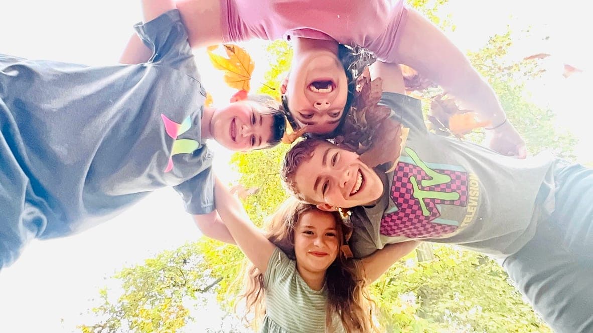 Four children in a circle seen from below, heads together against the sky.