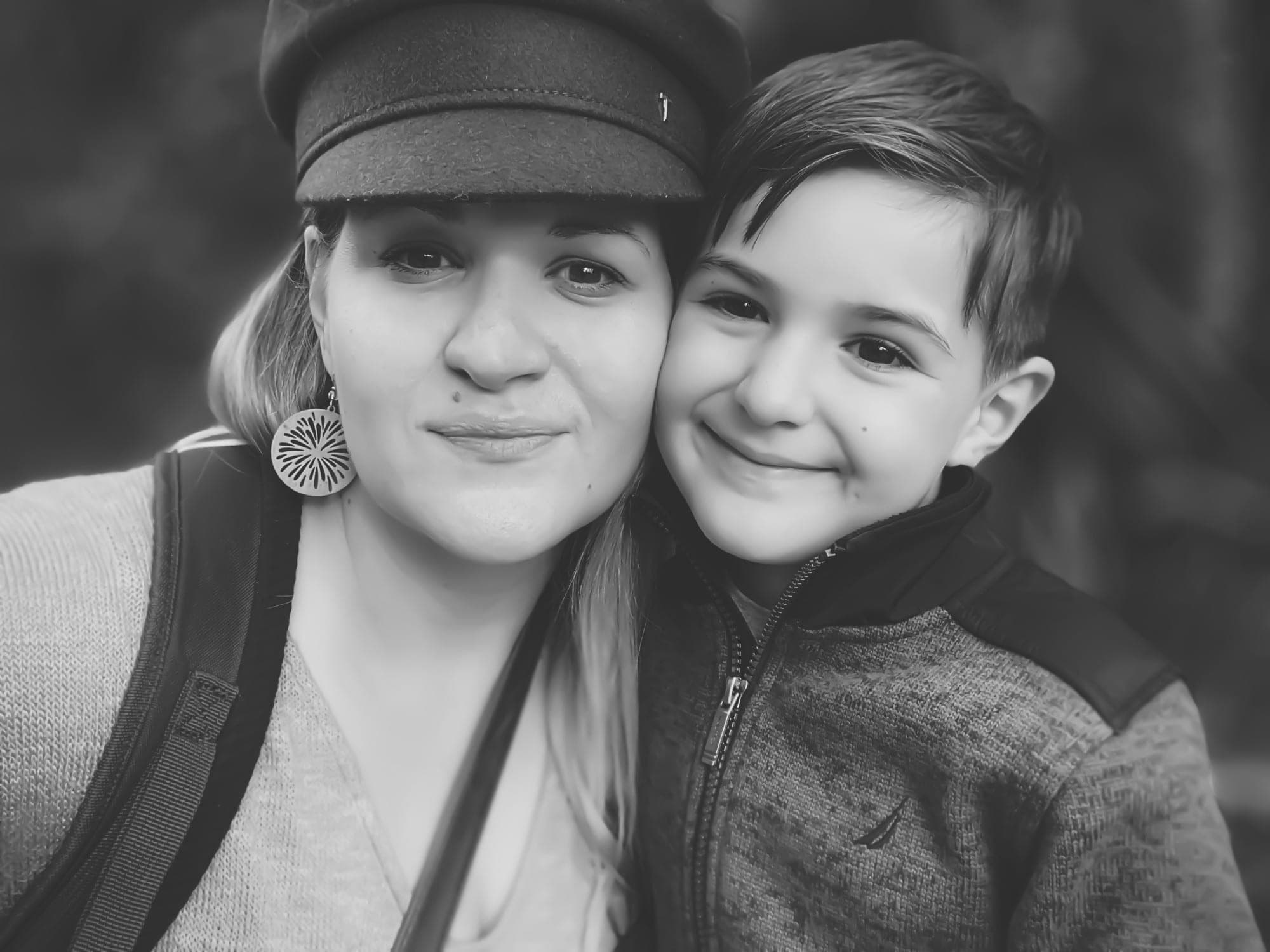 A woman in a wool cap and a boy, cheek to cheek, both looking straight at the camera. Black and white.