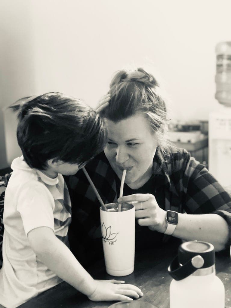 A boy and a young woman leaning into one milkshake at a diner table. Black and white.