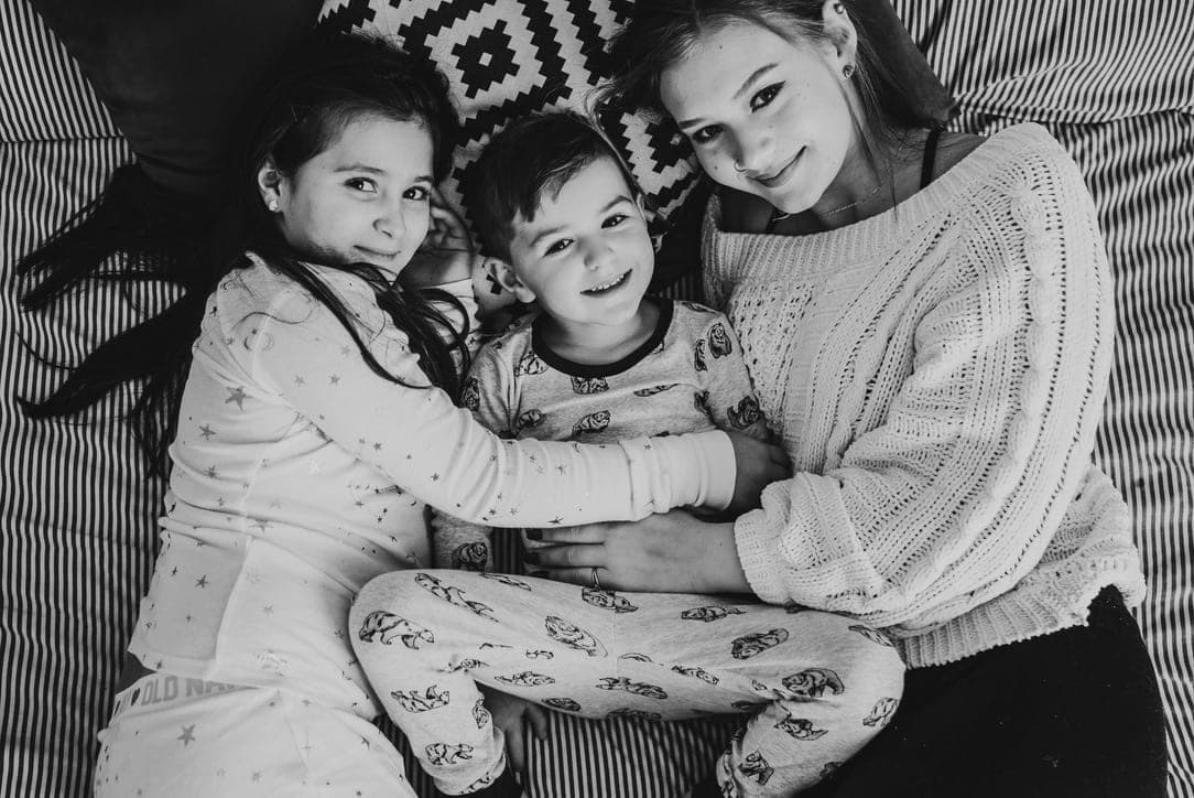 Three children in pyjamas on a striped bed, tangled together, looking up. Black and white.